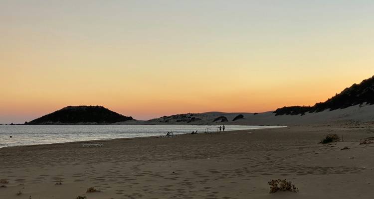 Plage au coucher du soleil avec des gens qui se promènent au bord de l'eau.