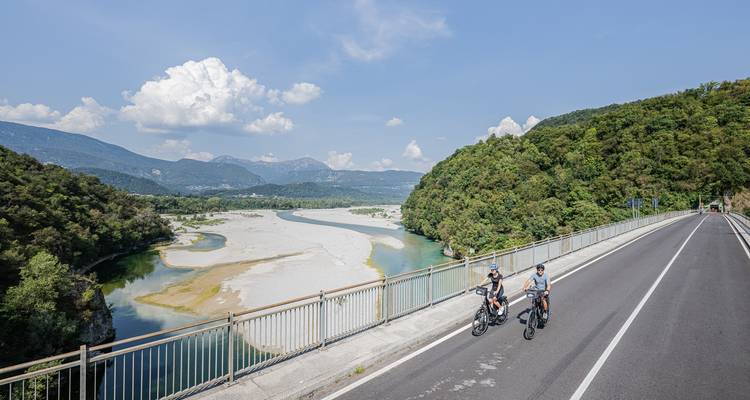 Cyclists on a bridge overlooking a river and mountains.