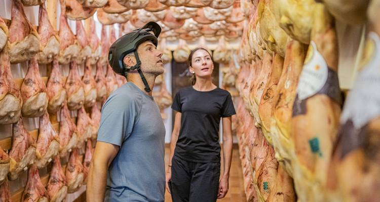 People observing hanging cured meats in a storage area.