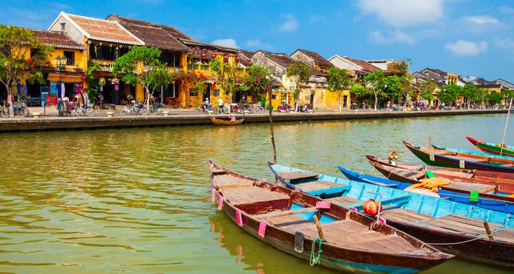 Colorful boats moored on a riverbank with traditional houses in the background.