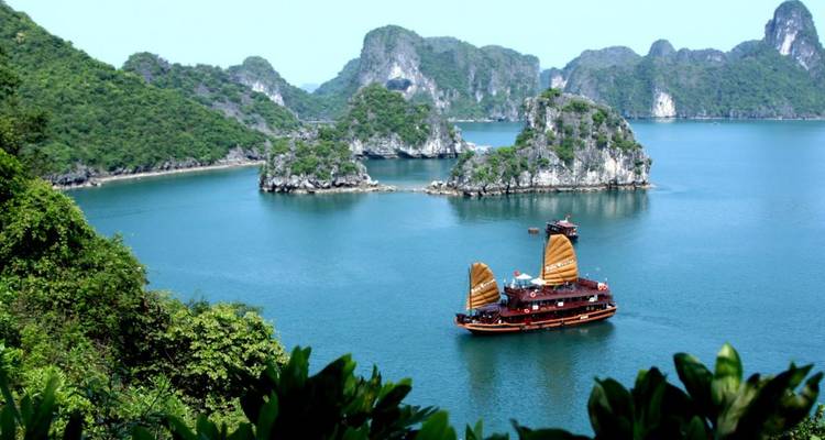 Traditional junk boat sailing in a tranquil bay surrounded by limestone cliffs.