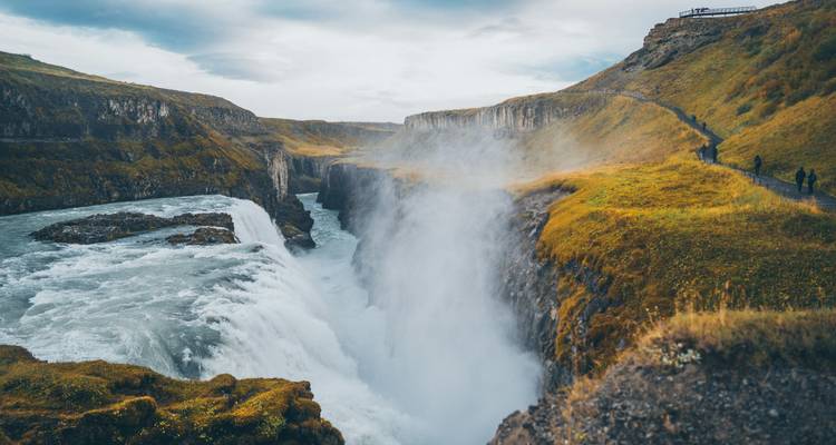 Massiver Wasserfall, der in eine Schlucht stürzt, mit Menschen auf einem Weg in der Nähe.