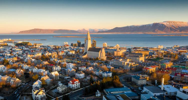 Luftaufnahme von Reykjavik mit einer großen Kirche, bunten Gebäuden, Meer und Bergen.