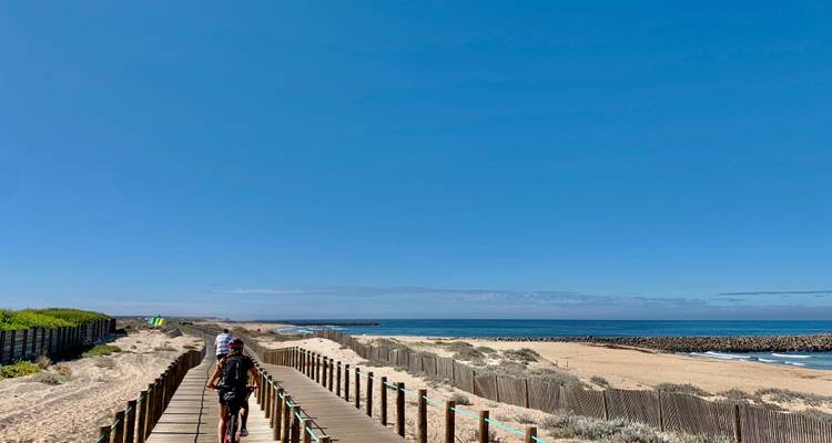 Cycliste sur une promenade en planches près d'une plage avec un ciel bleu clair.