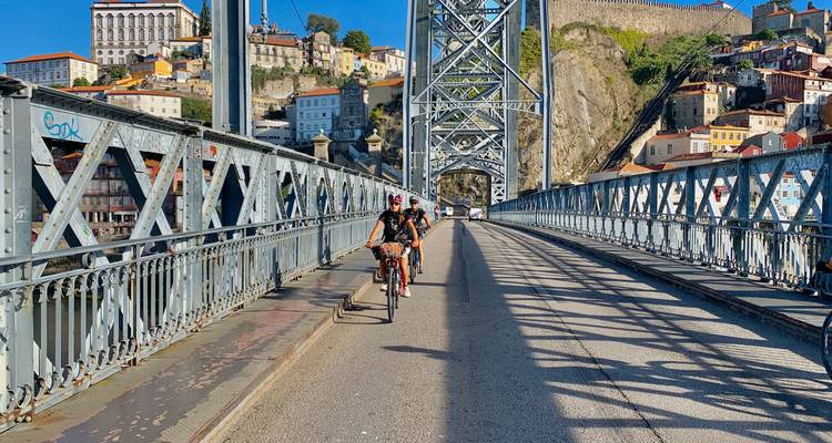 Cyclistes traversant un pont métallique avec un paysage urbain en arrière-plan.