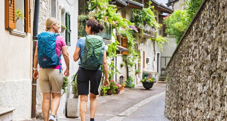 Deux randonneurs marchant dans une ruelle pittoresque avec des fleurs.