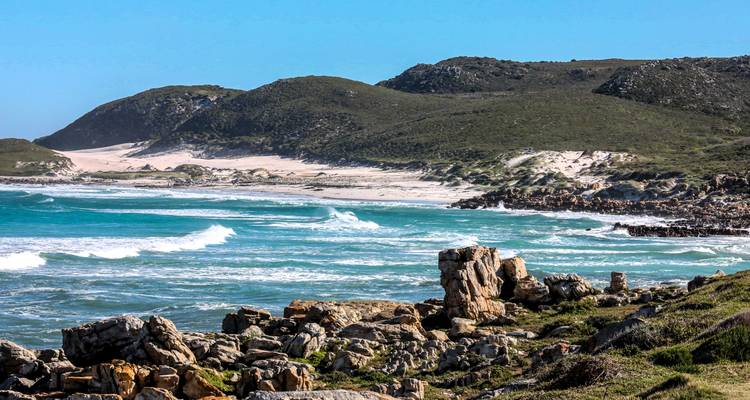 Côte rocheuse avec des vagues déferlantes et des collines verdoyantes.