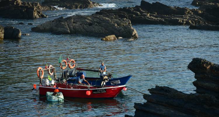 Pêcheurs sur un bateau dans des eaux côtières rocheuses.