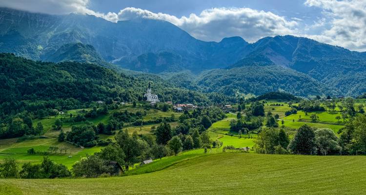 Une vue pittoresque d'une vallée verte avec une église et un village situés contre un terrain montagneux.