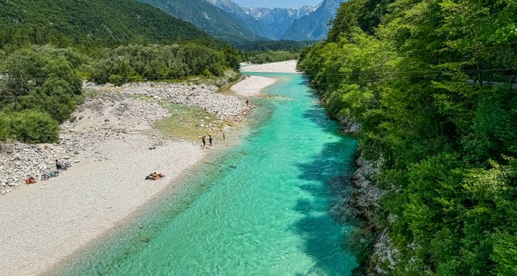 Une rivière turquoise qui traverse une vallée boisée avec des gens qui se détendent sur le lit de la rivière.