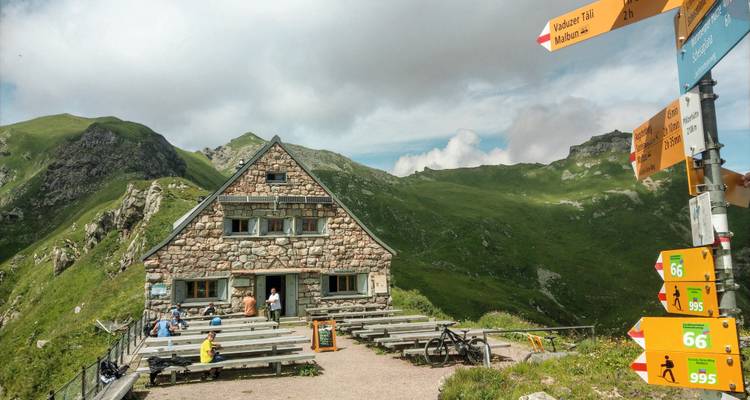 Refugio de montaña con bancos y señales direccionales en los Alpes.