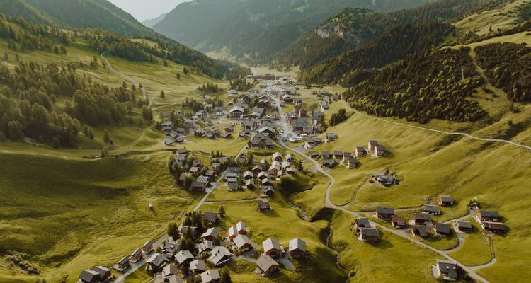 Vista aérea de un pequeño pueblo en un valle verde y exuberante rodeado de montañas.