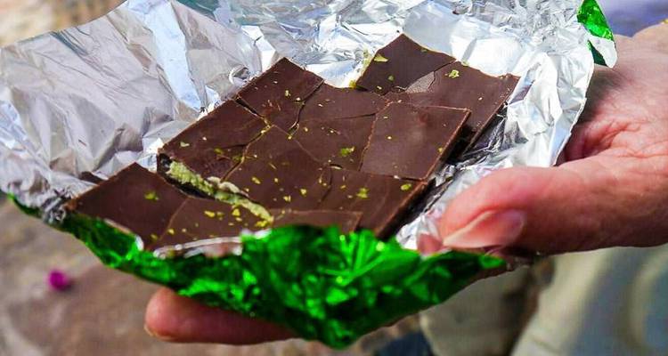 Hand holding chocolate wrapped in foil with spots of green.