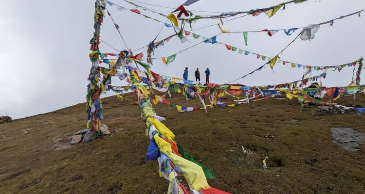 Des randonneurs debout parmi des drapeaux de prière colorés sur une colline.