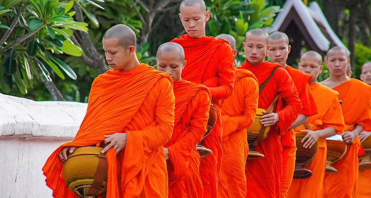 Une procession de moines en robes orange portant des bols à aumônes.