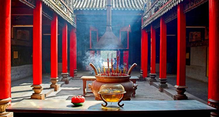 Intérieur d'un temple avec des colonnes rouges, de l'encens et des objets sacrés.