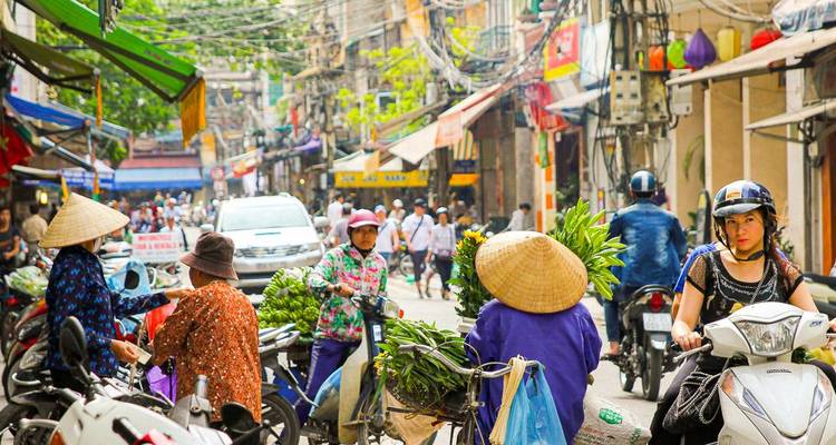Marché de rue animé avec des gens et des motos dans une zone urbaine.