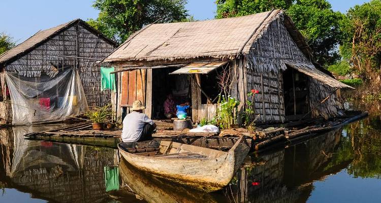 Personne dans un petit bateau sur l'eau près de maisons traditionnelles en bois.