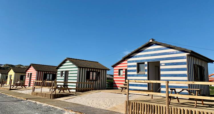 Kleurrijke gestreepte strandhuisjes onder een heldere hemel, met houten paden.