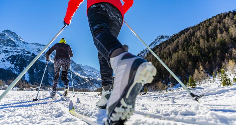 Deux personnes faisant du ski de fond dans un paysage montagneux enneigé.