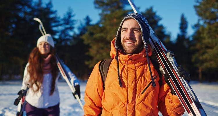 Couple marchant avec des skis sur un sentier enneigé sur fond d'arbres.
