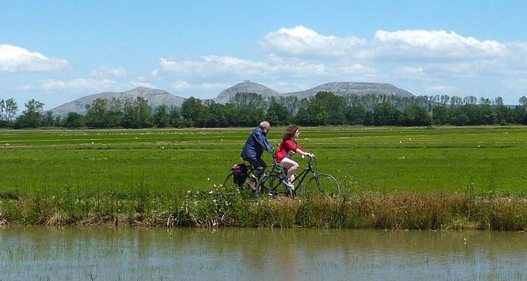 Deux personnes faisant du vélo sur un sentier le long d'un canal dans un paysage pittoresque.