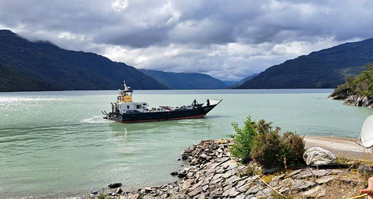Fähre auf einem See, umgeben von Bergen.