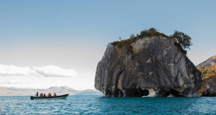 Boot mit Menschen nahe einer großen Felsformation im Wasser.