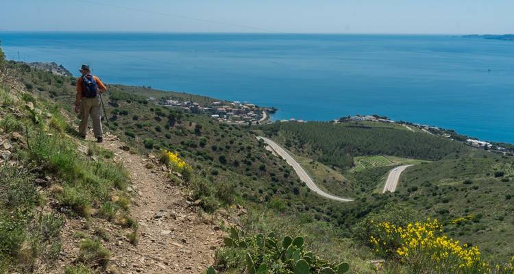 Randonneur marchant sur un sentier avec une vue panoramique d'une ville côtière.
