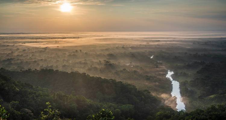 Ein atemberaubender Sonnenaufgang über dem Amazonas-Regenwald mit einem gewundenen Fluss und niedrigem Nebel.