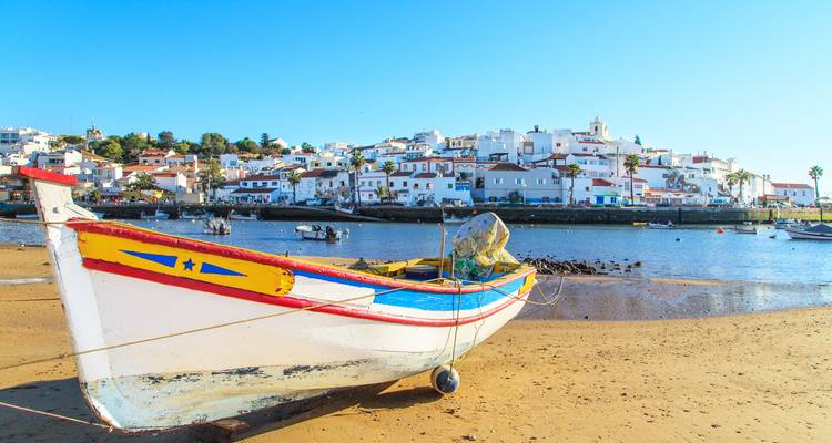 Traditional wooden boat on the shore with a coastal village in the background.
