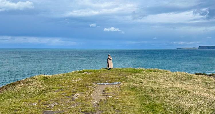 Person standing on a cliff by the sea under a cloudy sky.
