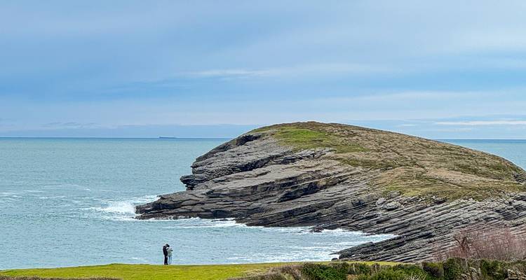 People standing and enjoying views by the sea near rocky cliffs.