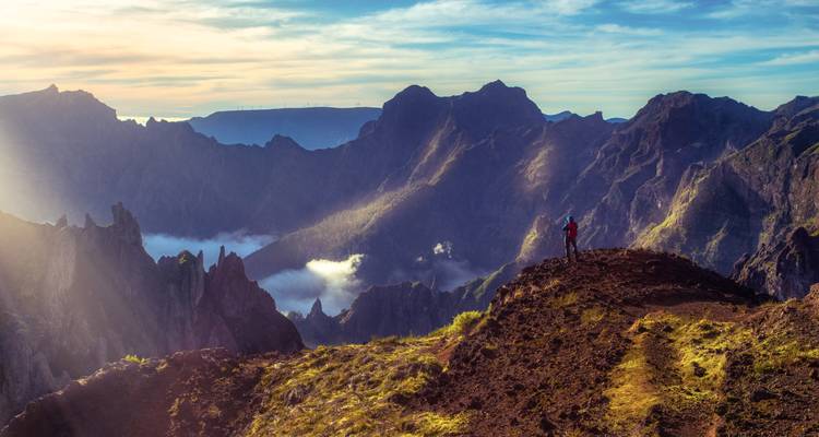 Vista panorámica de montañas escarpadas al amanecer con un excursionista disfrutando de la vista.