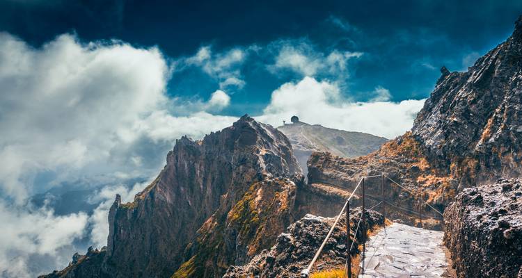 Un sendero rocoso de montaña con vista a un pico bajo un cielo nublado.