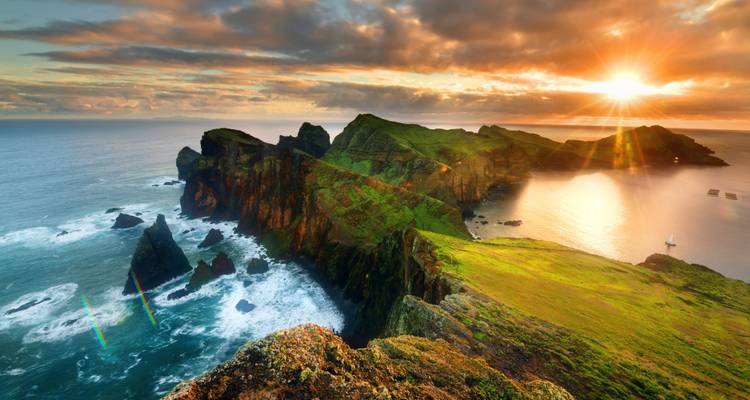 Una vista costera impresionante con acantilados y el sol poniéndose sobre el océano.
