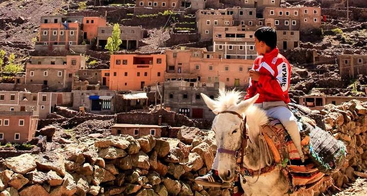 A boy riding a donkey overlooking a village built into a hillside.
