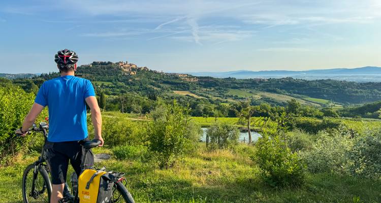 Radfahrer bewundert sanfte Weinberge und toskanische Hügelstadt, die in spätem Nachmittagslicht getaucht ist.