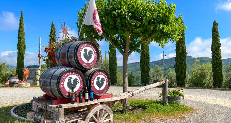 Chianti Classico Weinfässer auf rustikalem Wagen mit Zypressen und sanften Hügeln im Hintergrund.
