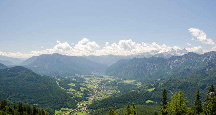 Panoramic view of a valley with a lake and surrounding mountains.