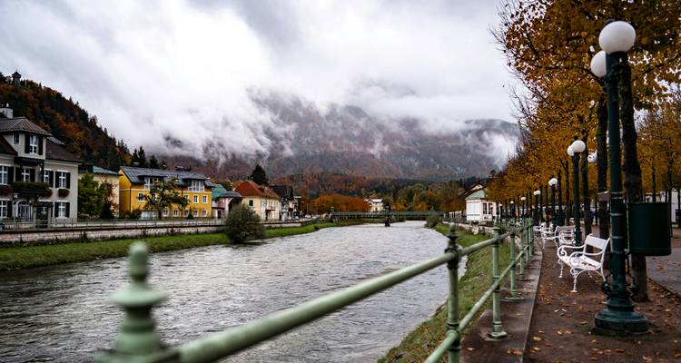 Mountain town by a river with autumn foliage, under cloudy skies.