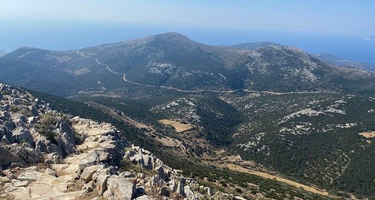 Paysage montagneux avec des sentiers rocheux et des collines lointaines.