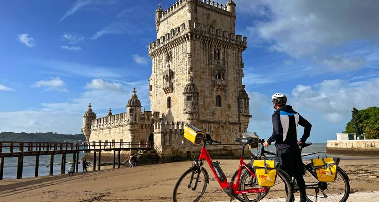 Radfahrer macht eine Pause neben dem historischen Turm von Belém am Tejo an einem klaren Morgen.
