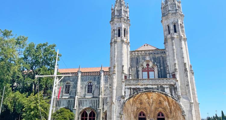 Neoklassische Basilika mit Zwillingstürmen erhebt sich gegen einen klaren blauen Himmel neben belaubten Bäumen.