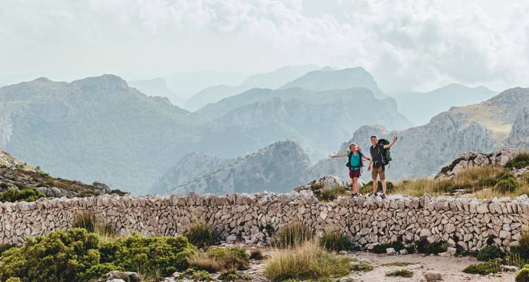 Randonneurs posant sur un mur de pierre avec des montagnes en arrière-plan.