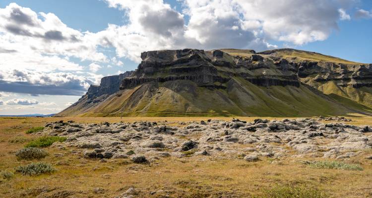 Eine flache, felsige Landschaft mit einer Kulisse aus steilen Klippen unter einem bewölkten Himmel.