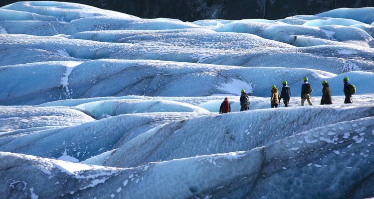 Groupe de personnes marchant sur un glacier glacé avec des casques et de l'équipement.