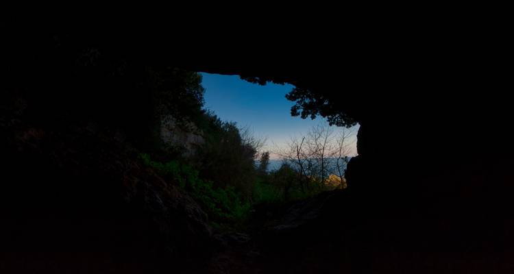 Una vista desde el interior de una cueva oscura mirando hacia un cielo brillante y un paisaje.