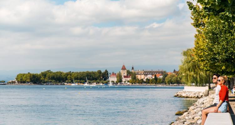 Deux personnes assises au bord d'un lac profitant de la vue d'une ville lointaine.