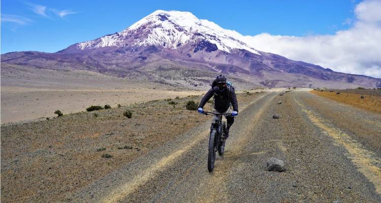 Un cycliste roulant sur une route déserte avec une majestueuse montagne enneigée en arrière-plan.